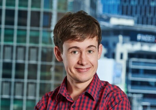 Will smiling with arms crossed tall buildings behind him.